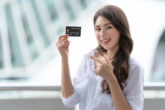 Femme tenant une carte de crédit et souriant près du magasin pendant le processus d'achat