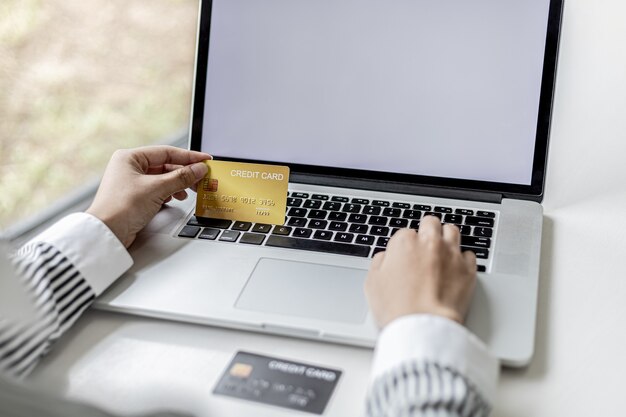 Femme tenant une carte de crédit et tapant sur un clavier d'ordinateur portable, elle remplit les informations de carte de crédit pour payer une commande sur un site d'achat sur Internet. Concept d'achat en ligne et de paiement par carte de crédit