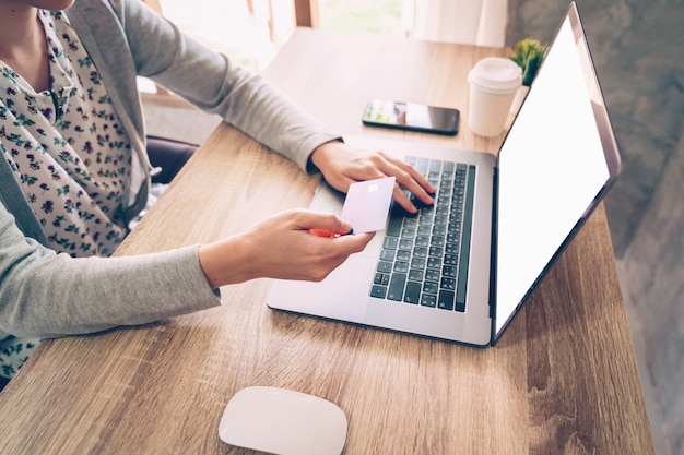 Femme tenant une carte de crédit tout en payant ses achats en ordinateur portable