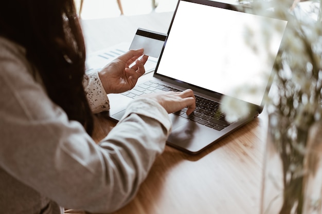 femme tenant une carte de crédit en utilisant un ordinateur portable pour faire du shopping en ligne.