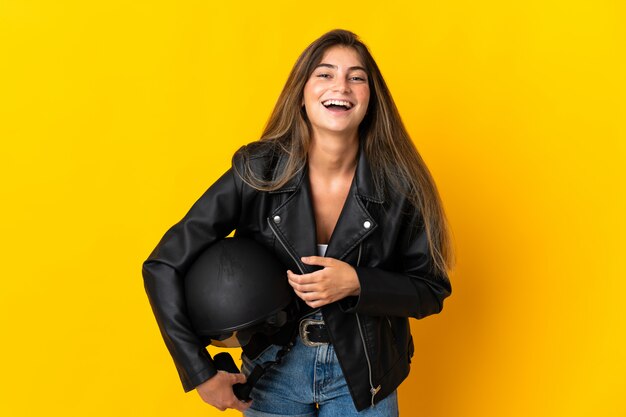 Femme tenant un casque de moto isolé sur jaune souriant beaucoup