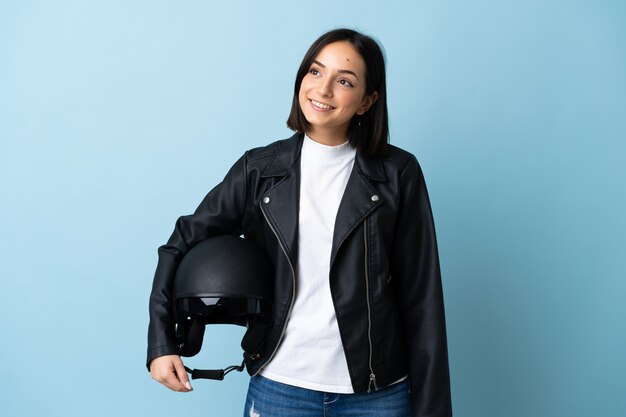 Femme tenant un casque de moto isolé sur un mur bleu en pensant à une idée tout en regardant