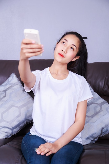 femme tenant un climatiseur de télécommande sur le canapé à la maison