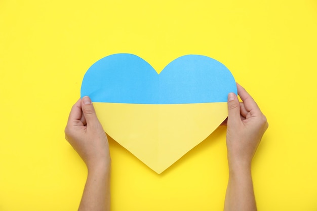 Femme tenant un coeur en papier aux couleurs du drapeau ukrainien sur la vue de dessus de fond jaune