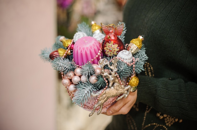 Femme tenant une composition de Noël en sapin, boules de verre colorées et jouets