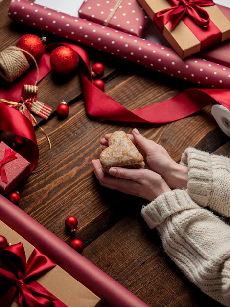 Femme tenant un cookie en forme de coeur sur une table en bois dans le temps d'emballage