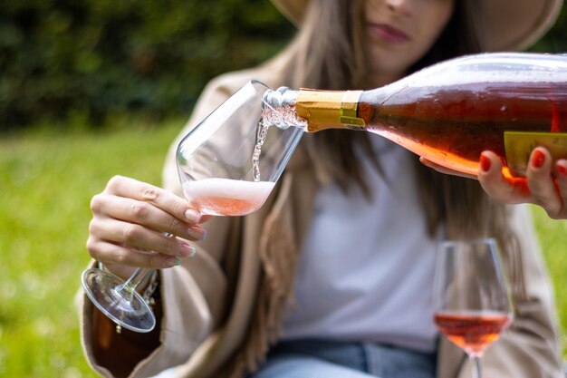 Une femme tenant une coupe en verre tout en se faisant servir du champagne rouge à l'extérieur dans le parc