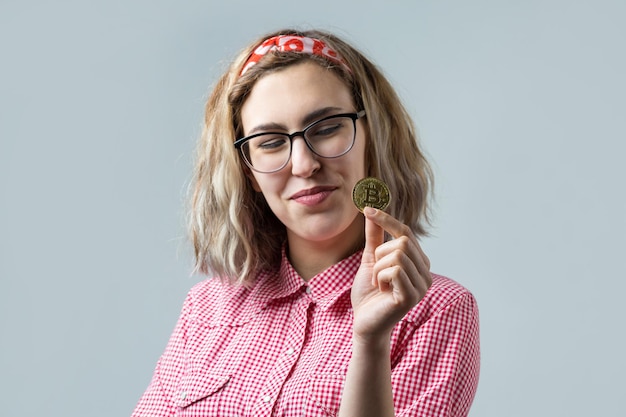 Femme tenant une crypto-monnaie bitcoin physique dans sa main sur fond gris