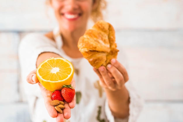 Une femme tenant dans une main une orange et plus de fruits et de l'autre, elle a un croissant - choisissant un mode de vie et un concept de régime