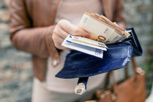 Photo femme tenant dans les mains un portefeuille avec de l'argent en euros une fille de la ville sort de l'argent du portefeuille