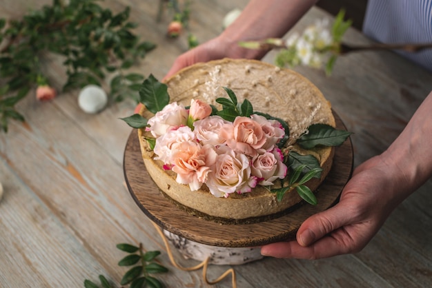 Femme tenant dans ses mains un beau gâteau mousse crue décoré de fleurs de tendresse