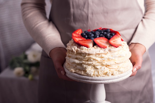 Femme tenant dans ses mains le fameux gâteau aux fraises Pavlova