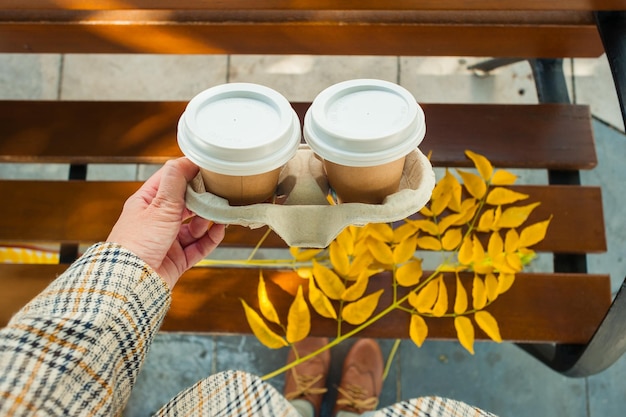 Une femme tenant deux tasses de café à emporter en automne dans la ville portant des vêtements vintage.