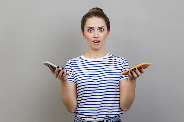 Femme tenant deux téléphones portables regardant la caméra avec de grands yeux et la bouche ouverte