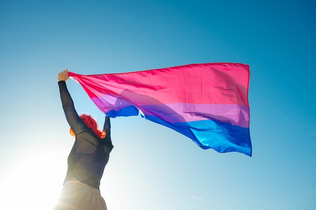 Femme tenant le drapeau arc-en-ciel bisexuel avec le ciel bleu