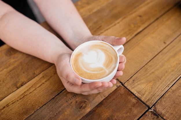 Femme tenant du café latte art sur une table en bois dans un café