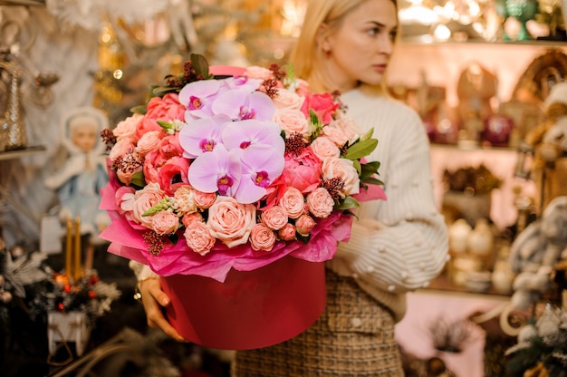 Femme tenant une énorme boîte rouge avec des roses de couleur pêche, des orchidées rose clair et une autre fleur de couleur rose