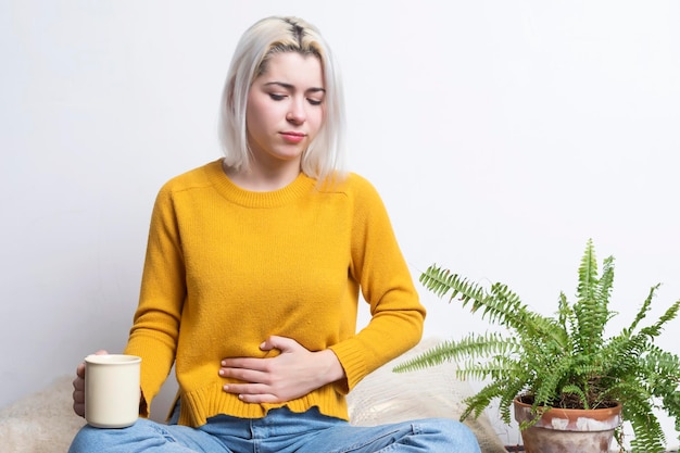 Photo femme tenant l'estomac alors qu'elle est assise contre le mur