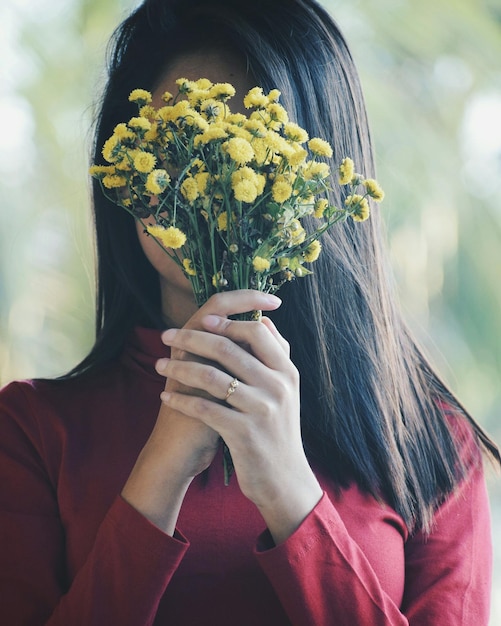 Une femme tenant des fleurs devant son visage.