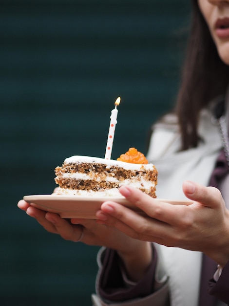 Une femme tenant un gâteau d'anniversaire avec une bougie d'annivernais sur une assiette beige