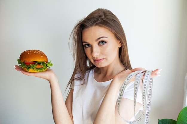 Femme tenant un hamburger malsain avec un ruban à mesurer dans la cuisine