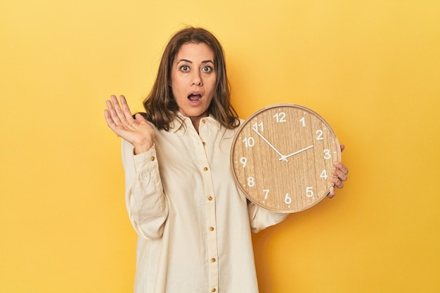 Photo femme tenant une horloge sur fond jaune surprise et choquée