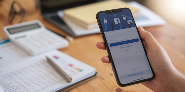 Femme tenant un iPhone X avec le service Internet social Facebook à l'écran.