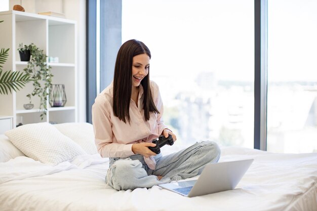 Une femme tenant un joystick sans fil en jouant à des jeux vidéo sur un ordinateur portable moderne