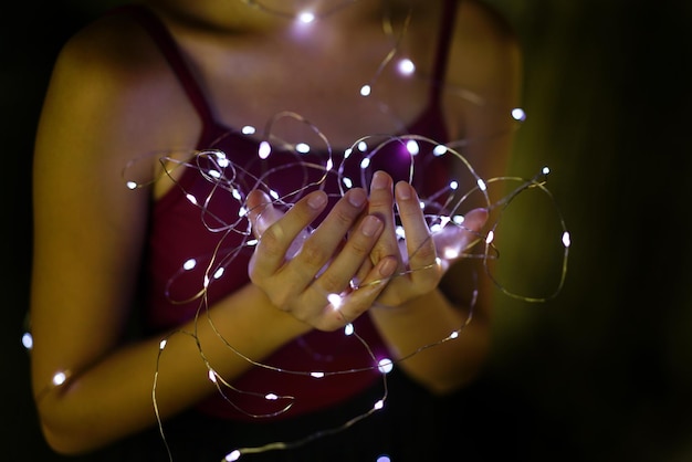 Photo femme tenant une lampe à cordes éclairée dans une chambre noire