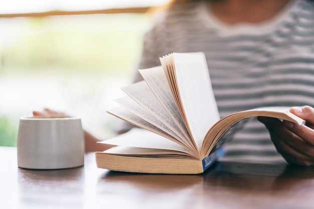 femme tenant et lisant un livre tout en buvant du café sur la table en bois