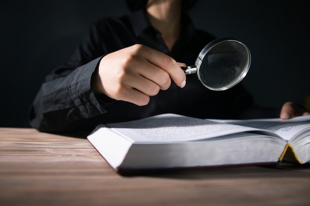 Femme tenant une loupe et un livre de lecture sur fond sombre