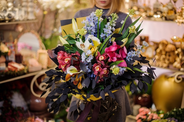 Femme tenant un magnifique bouquet d'orchidées, de lys et de belles feuilles