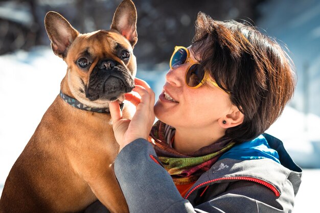 Femme tenant sur les mains le buldog français et jouant avec sur le fond blanc neigeux