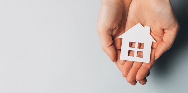 Femme tenant une maison de papier avec ses mains avec le soleil sur un espace bleu clair