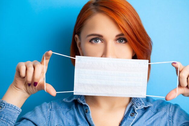 Femme tenant un masque pour couvrir la bouche et le nez pour se protéger contre les virus sur fond bleu.