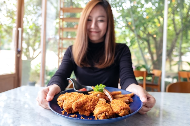 Une femme tenant et montrant une assiette de poulet frit et frites au restaurant