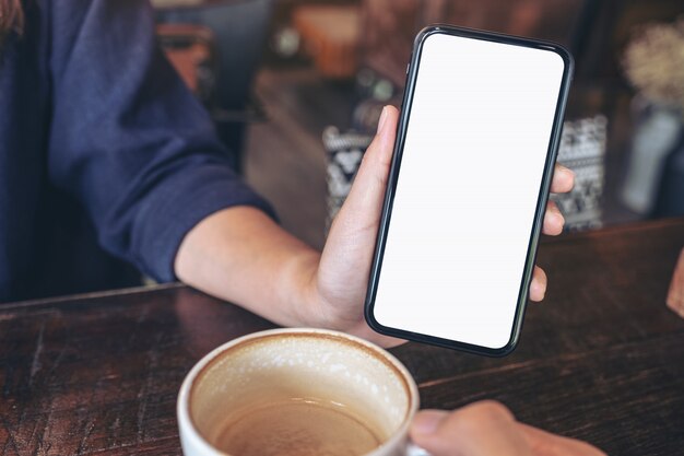 Une femme tenant et montrant un téléphone mobile noir avec écran vide à quelqu'un sur la table au café