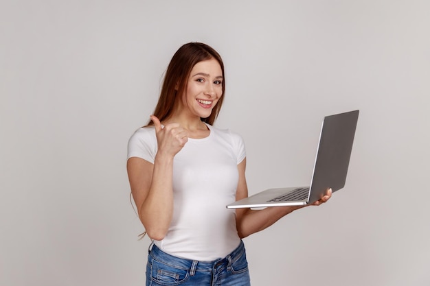 Femme tenant un ordinateur portable et montrant les pouces regardant la caméra ayant une conférence en ligne à l'aide d'un ordinateur