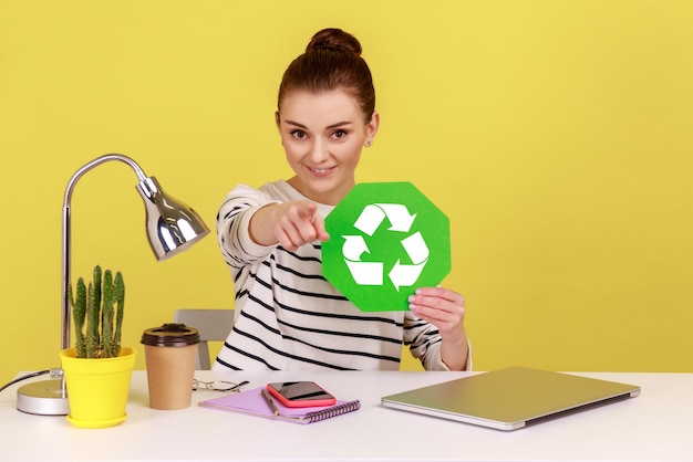 Femme tenant une pancarte verte de recyclage dans la main et pointant le doigt vers la caméra