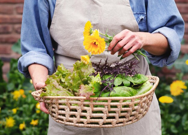 Une femme tenant un panier de légumes frais et de fleurs dans un jardin urbain