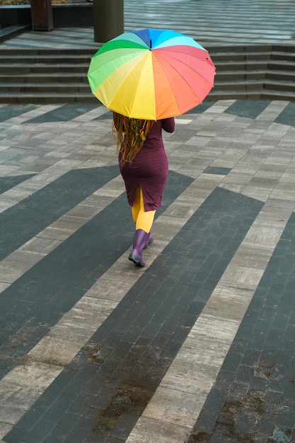 Une femme tenant un parapluie arc-en-ciel dans la ville pendant qu'il pleut