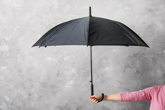 Femme tenant un parapluie noir sur un fond gris