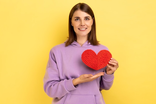 Femme tenant un petit coeur en papier rouge et souriant à la caméra célébrant la saint valentin