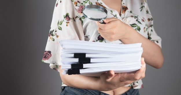 Femme tenant une pile de documents d'étude avec une loupe