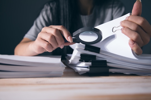 Femme tenant une pile de papiers sur la table. étudier avec une loupe