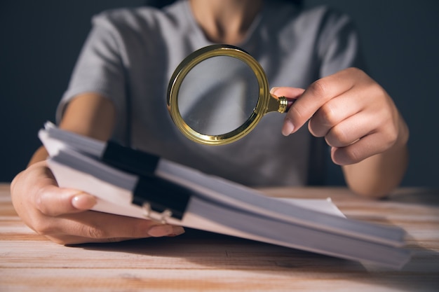 Femme tenant une pile de papiers sur la table. étudier avec une loupe