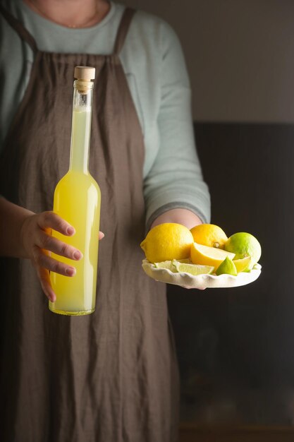 Femme tenant un plat de citron et de citron vert et une bouteille de boisson maison verticale de style rustique