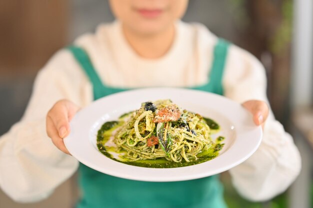 Photo une femme tenant un plat de savoureux spaghettis avec sauce pesto concept d'alimentation saine