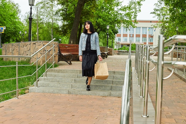 Femme tenant plusieurs sacs en papier marchant à l'extérieur dans le parc