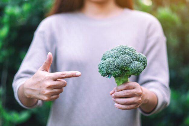 Une femme tenant et pointant du doigt un brocoli vert frais